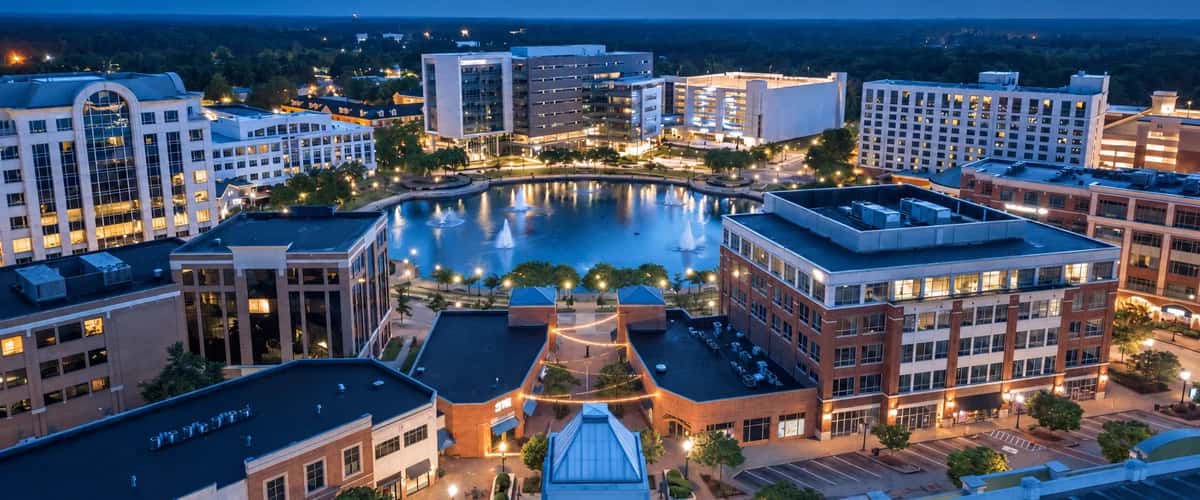 Newport News cityscape at twilight, with illuminated buildings surrounding a lake and fountains