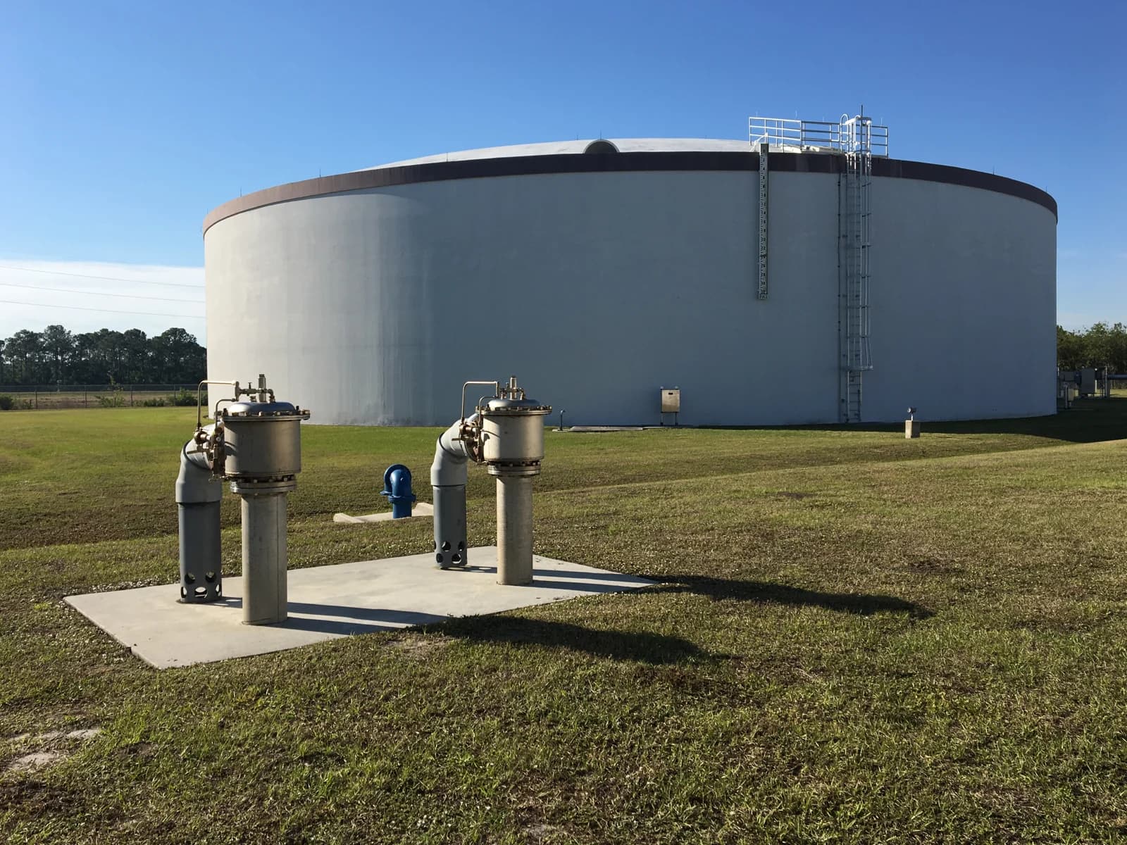 Ground-level circular water storage tank with access ladder and pipework