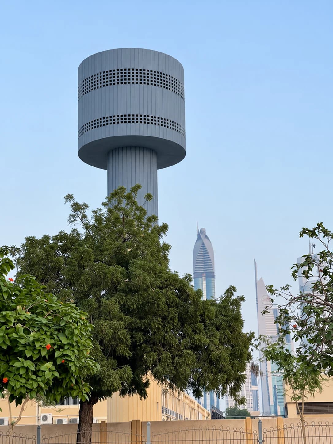 Blue-gray elevated water tower rising above trees with a city skyline in the background