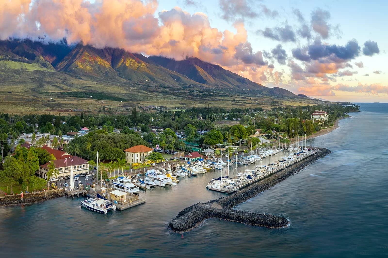 Maui coastline with a boat harbor beneath green mountains and sunset clouds