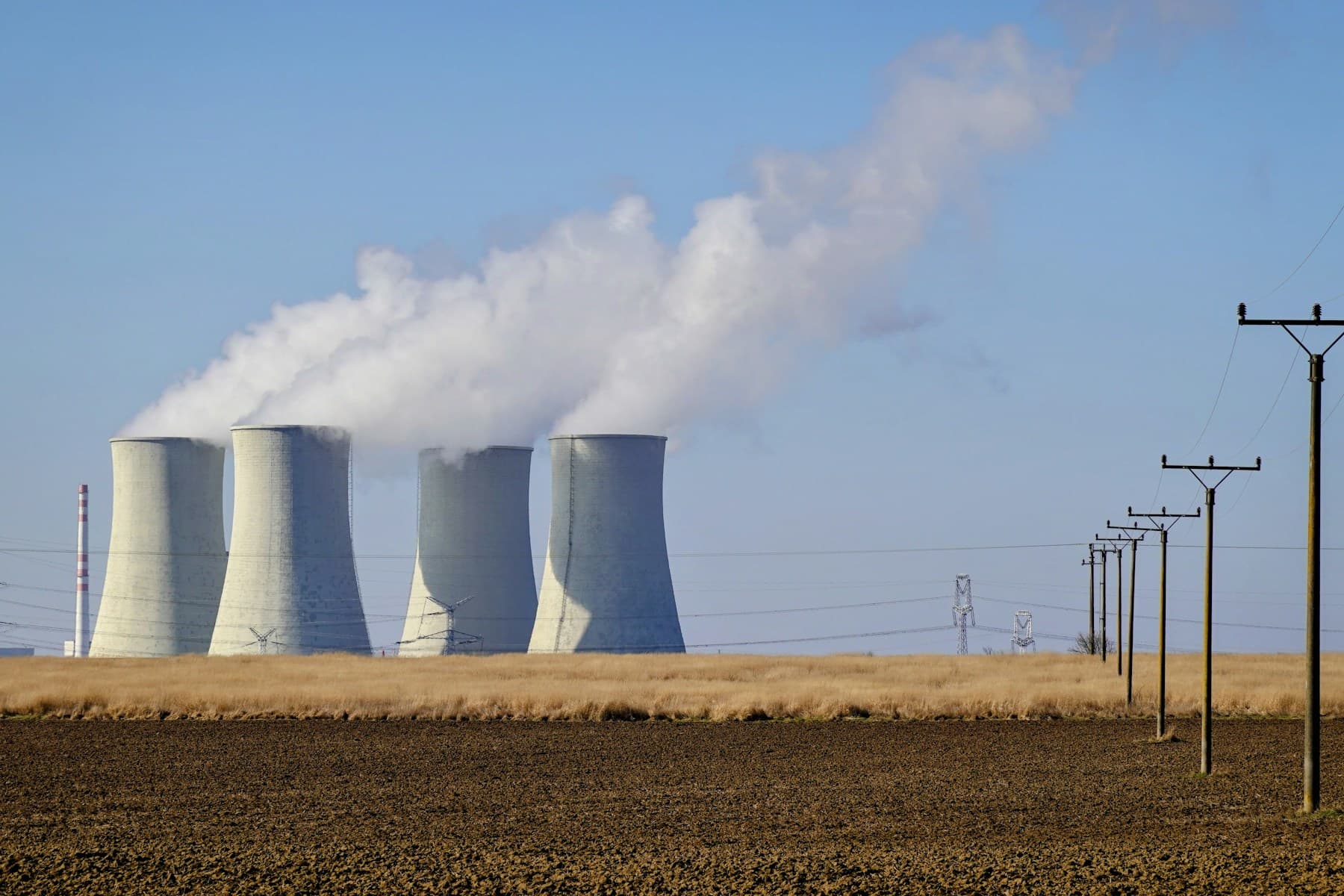 Power station with four large concrete cooling towers releasing steam beside electrical transmission lines